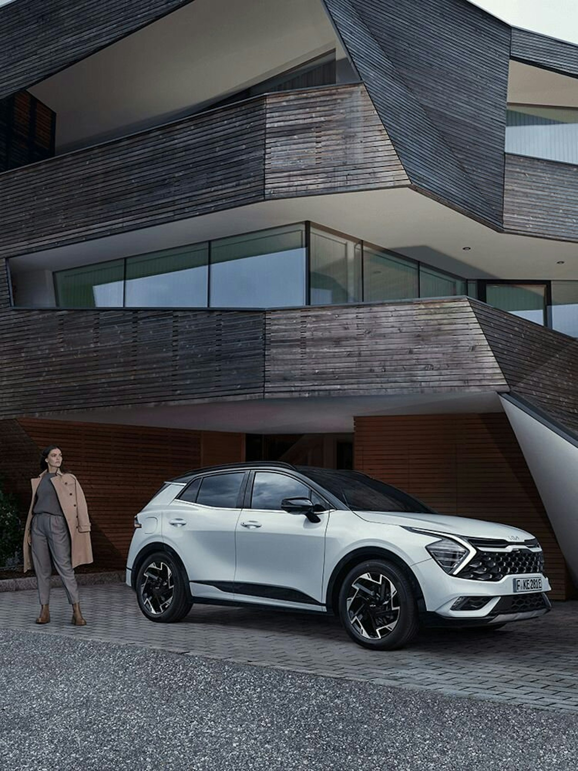 Eine Frau steht mit dem Kia Sportage vor einem Haus