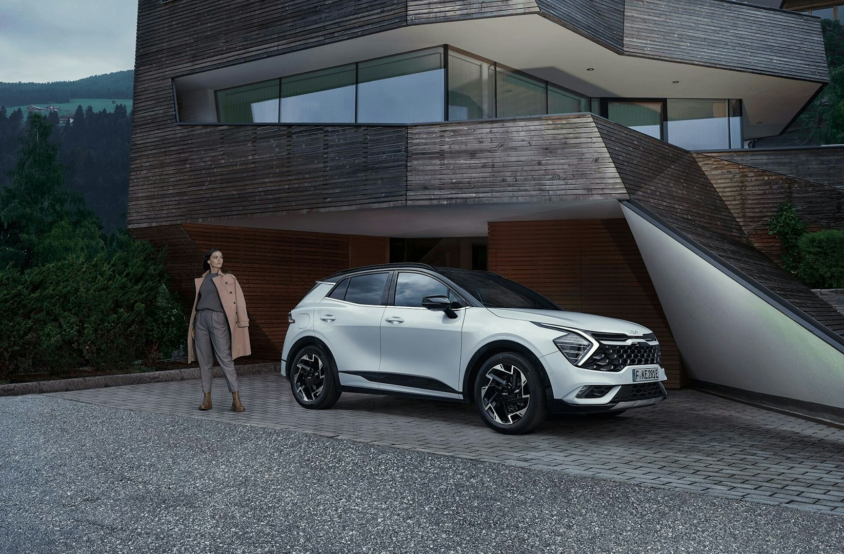 Eine Frau steht mit dem Kia Sportage vor einem Haus